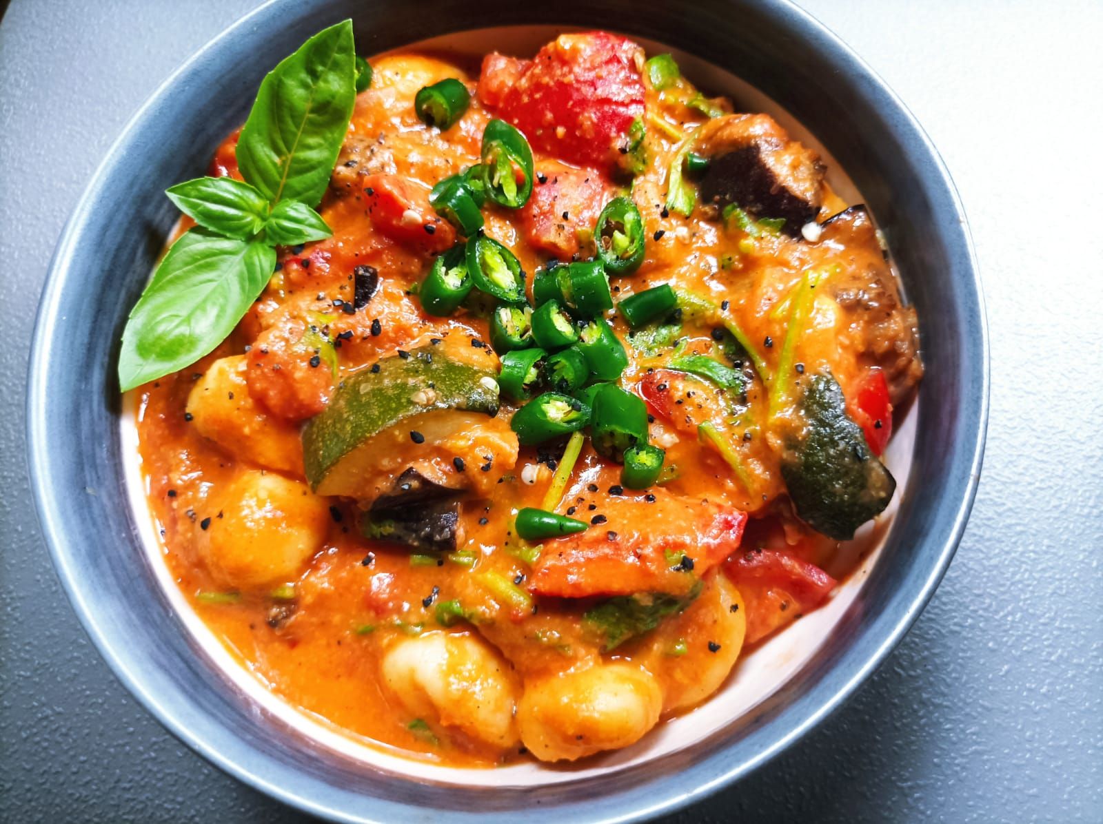 Roasted Vegetable Gnocchi in a bowl topped with basil leaves and fresh cut chili pepper