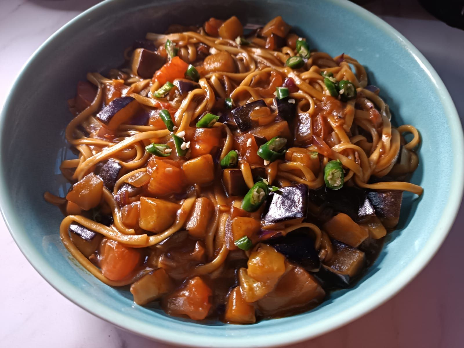 aubergine and noodle stir-fry topped with sliced green chili