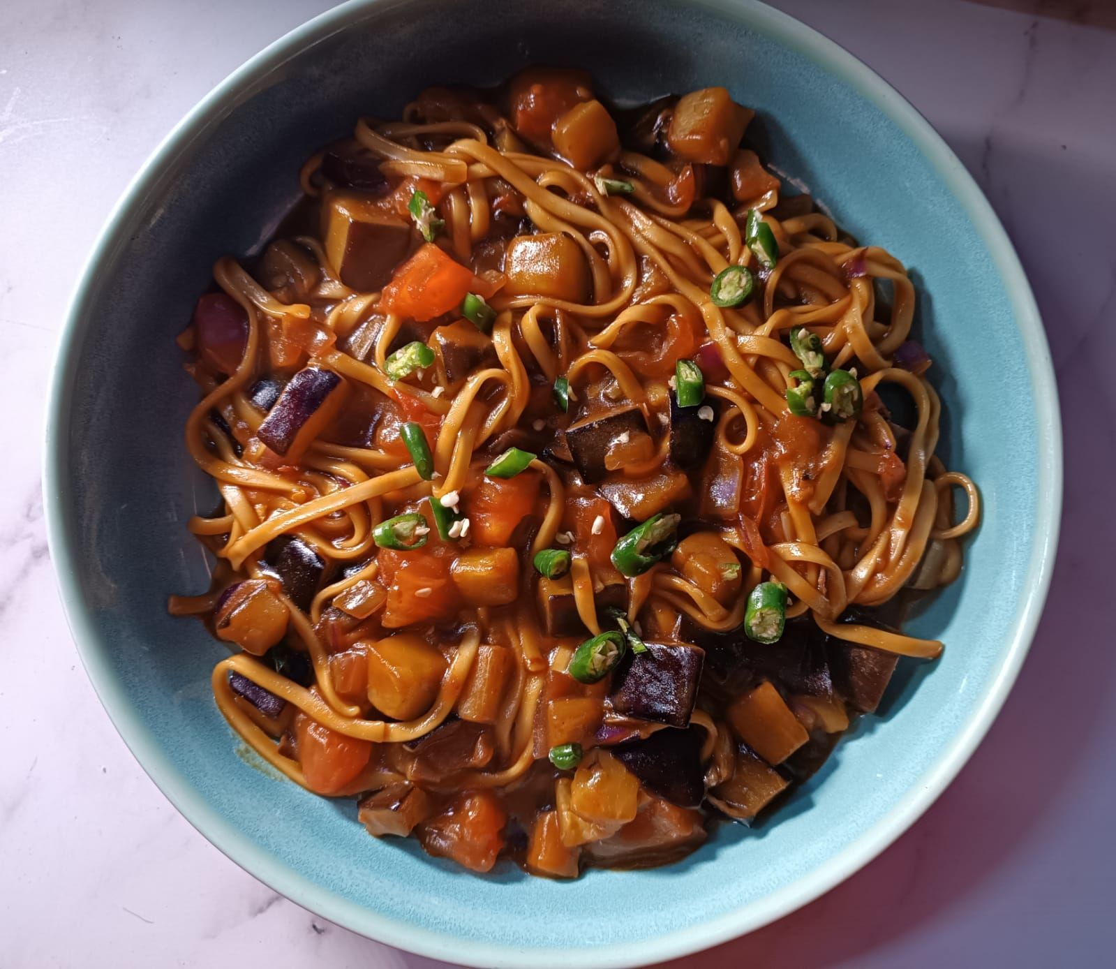 aubergine and noodle stir-fry topped with sliced green chili