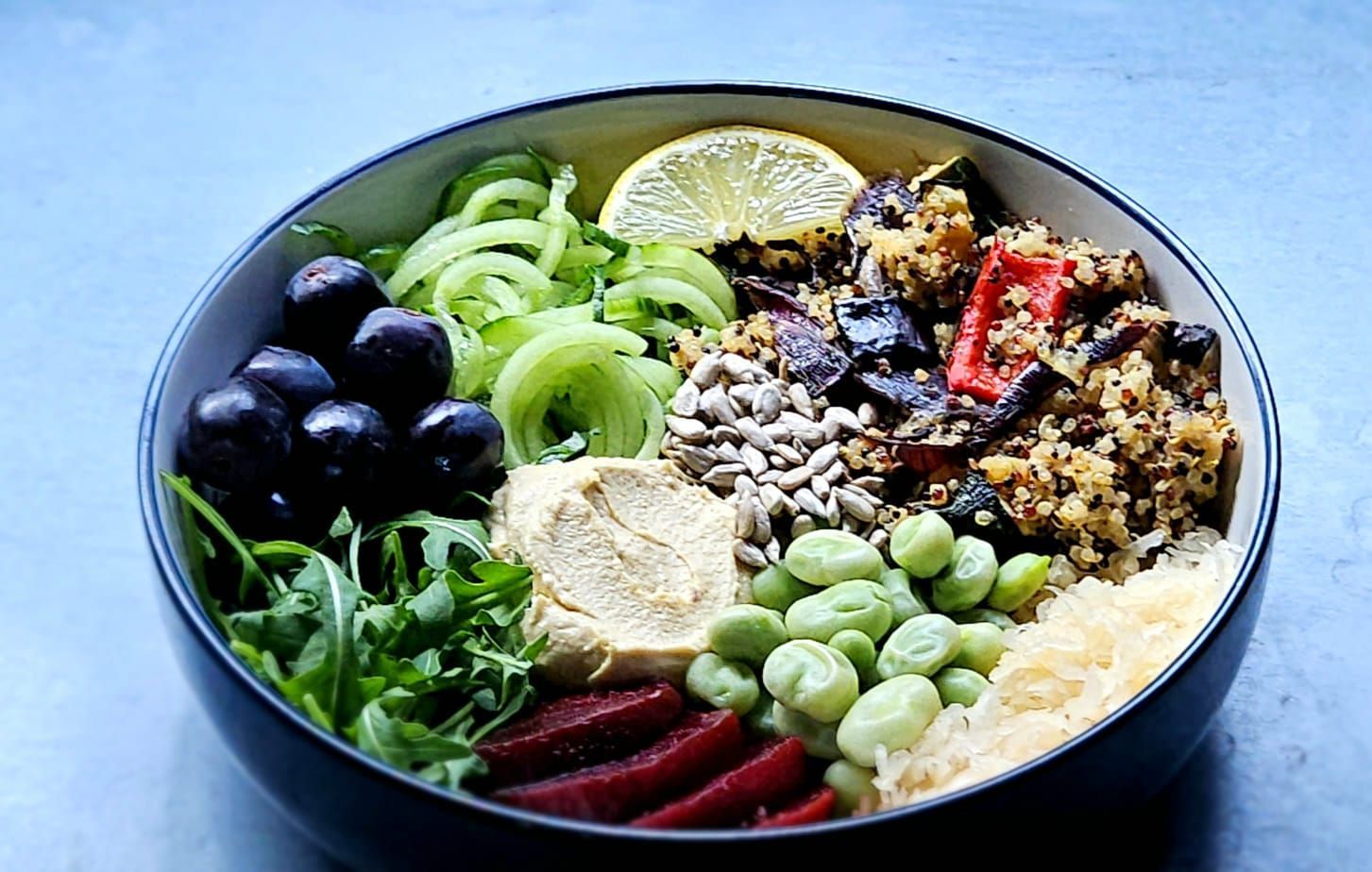 bowl of grain salad with hummus grapes, cucumber noodles, fava beans, and roasted vegetable quinoa salad