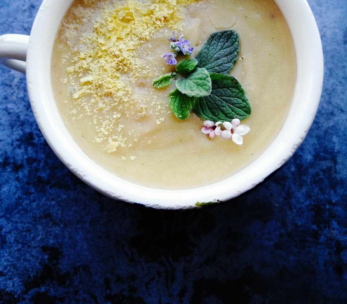 lentil soup in a cup topped with oregano, tiny pink flowers, and nutritional yeast