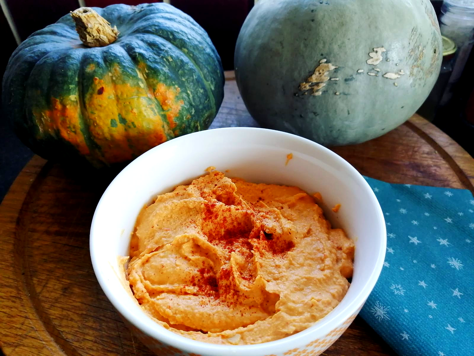 Red pepper hummus in a bowl with pumpkins in the background