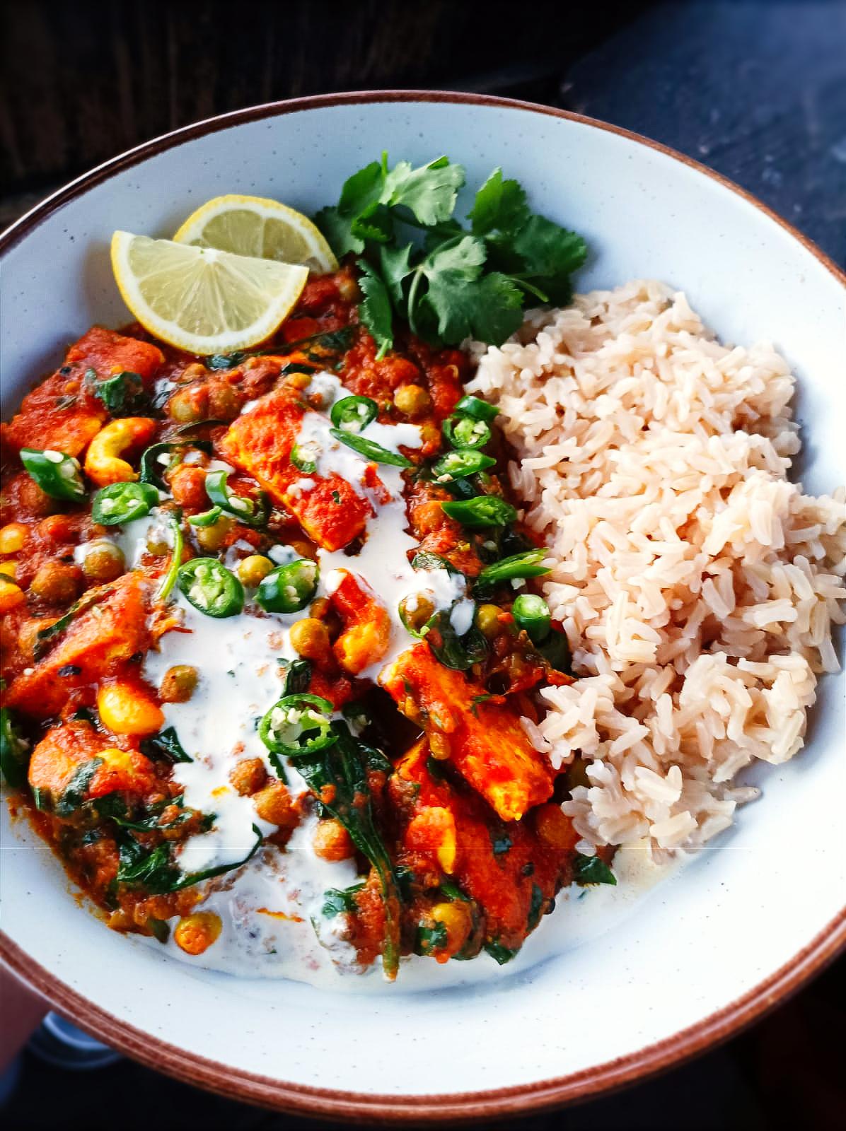 close up photo of a tofu tikka curry served with brown rice and a tomato sauce
