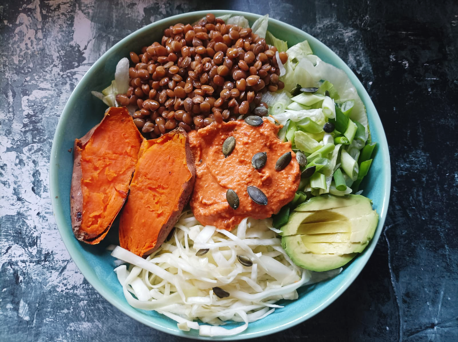buddha bowl containing lentils, sweet potato, salad and half of an avocado in a bowl with a dark and light background