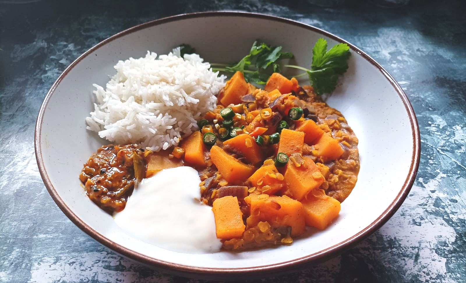 Cubes of butternut squash with lentil dal served with rice, fresh coriander, mixed pickle, and coconut yogurt
