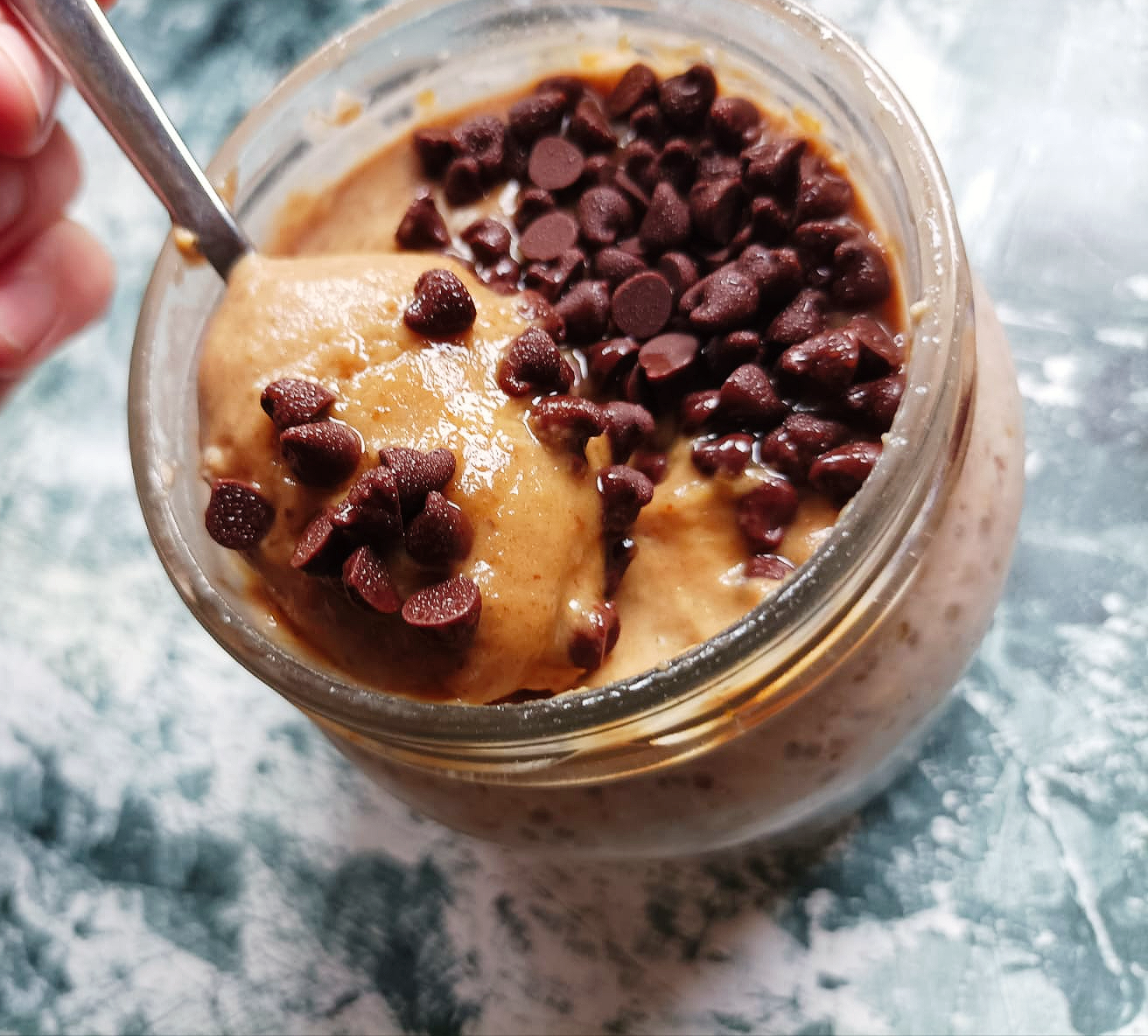 a spoon diving into a jar filled with salted caramel overnight oats and topped with chocolate chips
