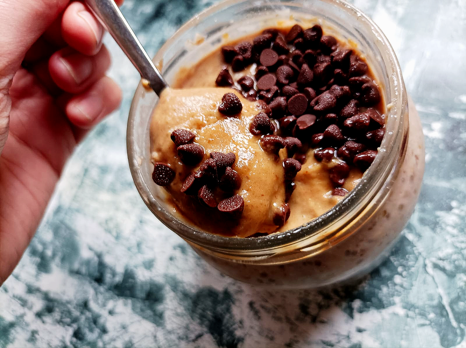 a spoon diving into a jar filled with salted caramel overnight oats and topped with chocolate chips