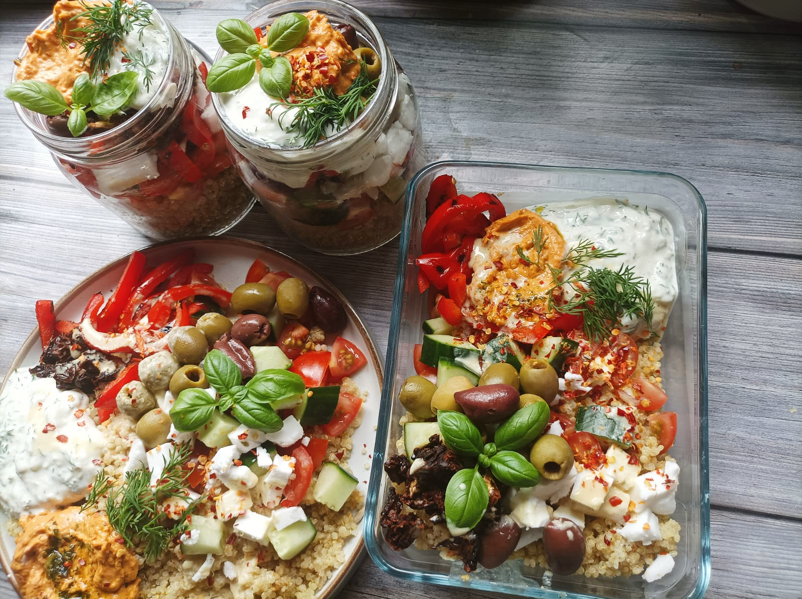 4 servings of Mediterranean quinoa salad with two jar servings, one glass dish, and one bowl all filled with quinoa, vegan feta, veggies, hummus and tzatziki