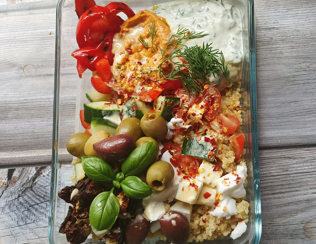 a dish of quinoa salad with veggies, vegan feta, fresh basil, hummus and tzatziki