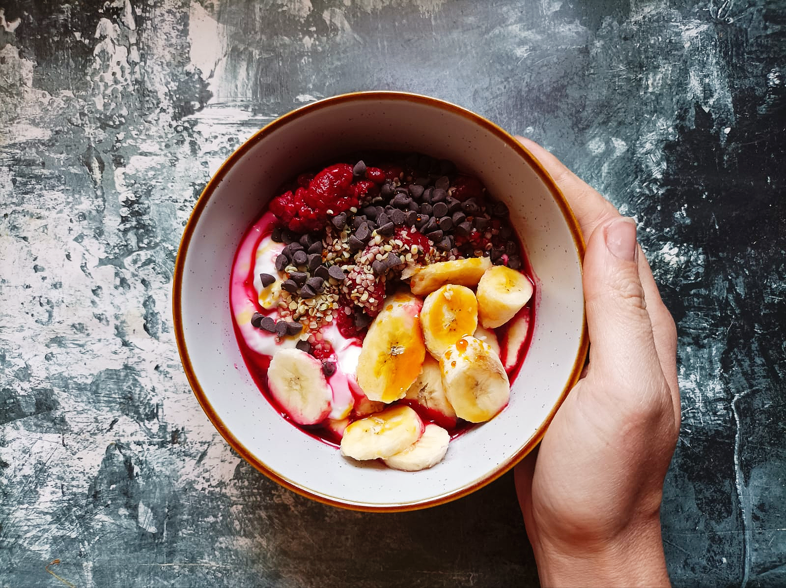 fruit in a bowl with yogurt and chocolate chips and a hand holding the bowl