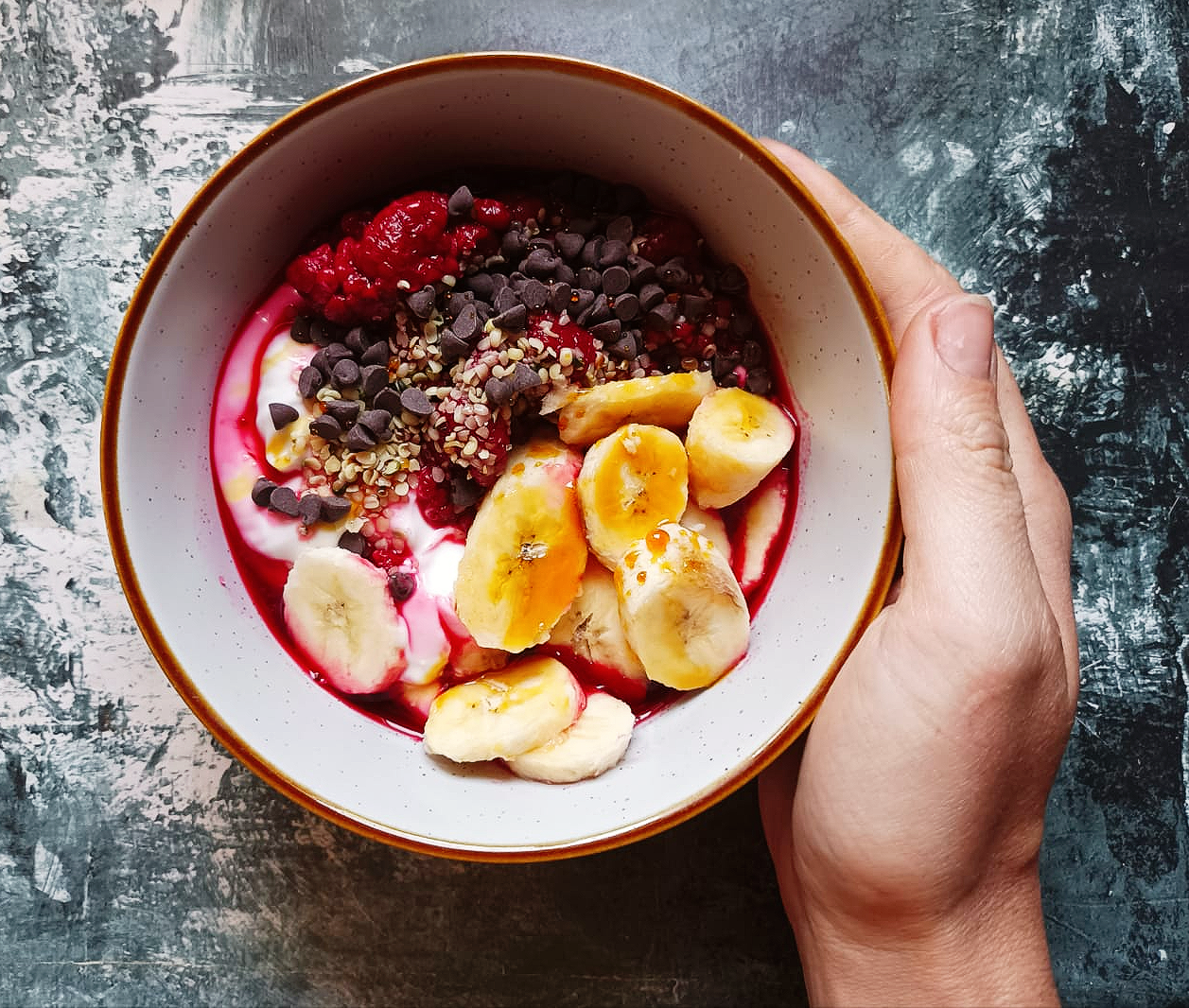 fruit in a bowl with yogurt and chocolate chips and a hand holding the bowl