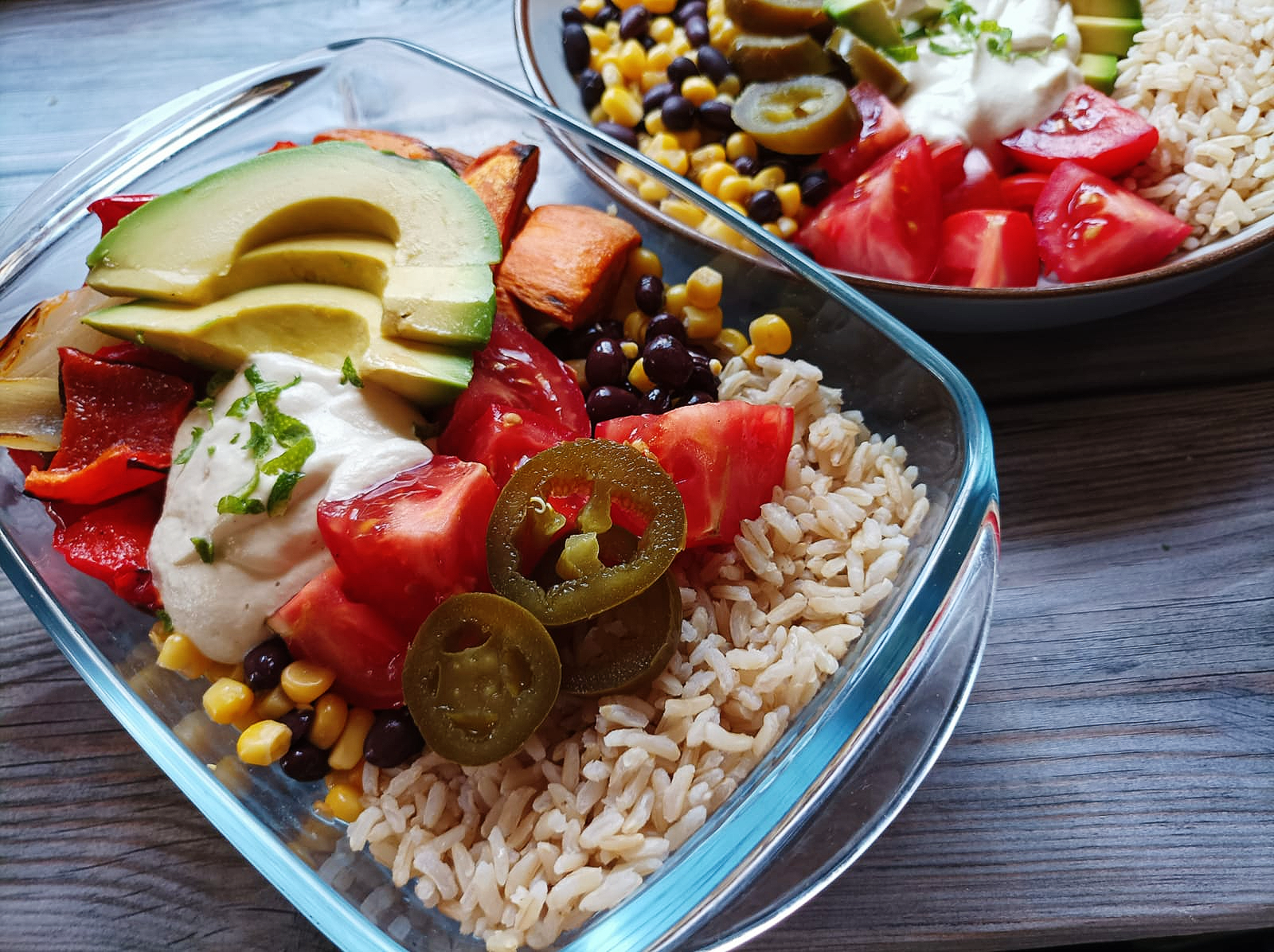 Buddha bowl made with rice and black beans, topped with roasted veg, tomatoes, avocado, cashew cream