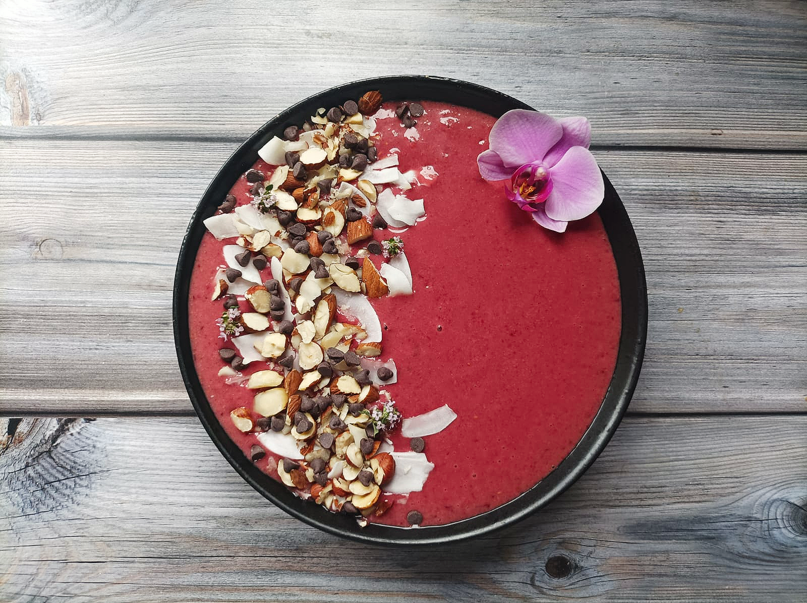 Cherry smoothie bowl topped with chopped nuts, coconut, and chocolate chips