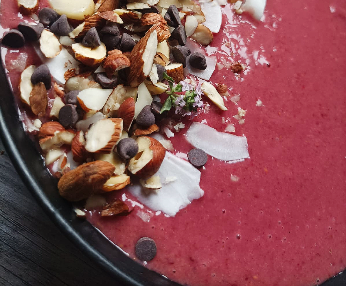 Cherry smoothie bowl topped with chopped nuts, coconut, and chocolate chips