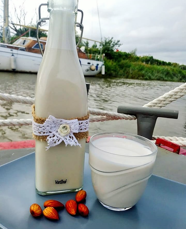 a bottle and glass filled with almond milk a boat and river in the background