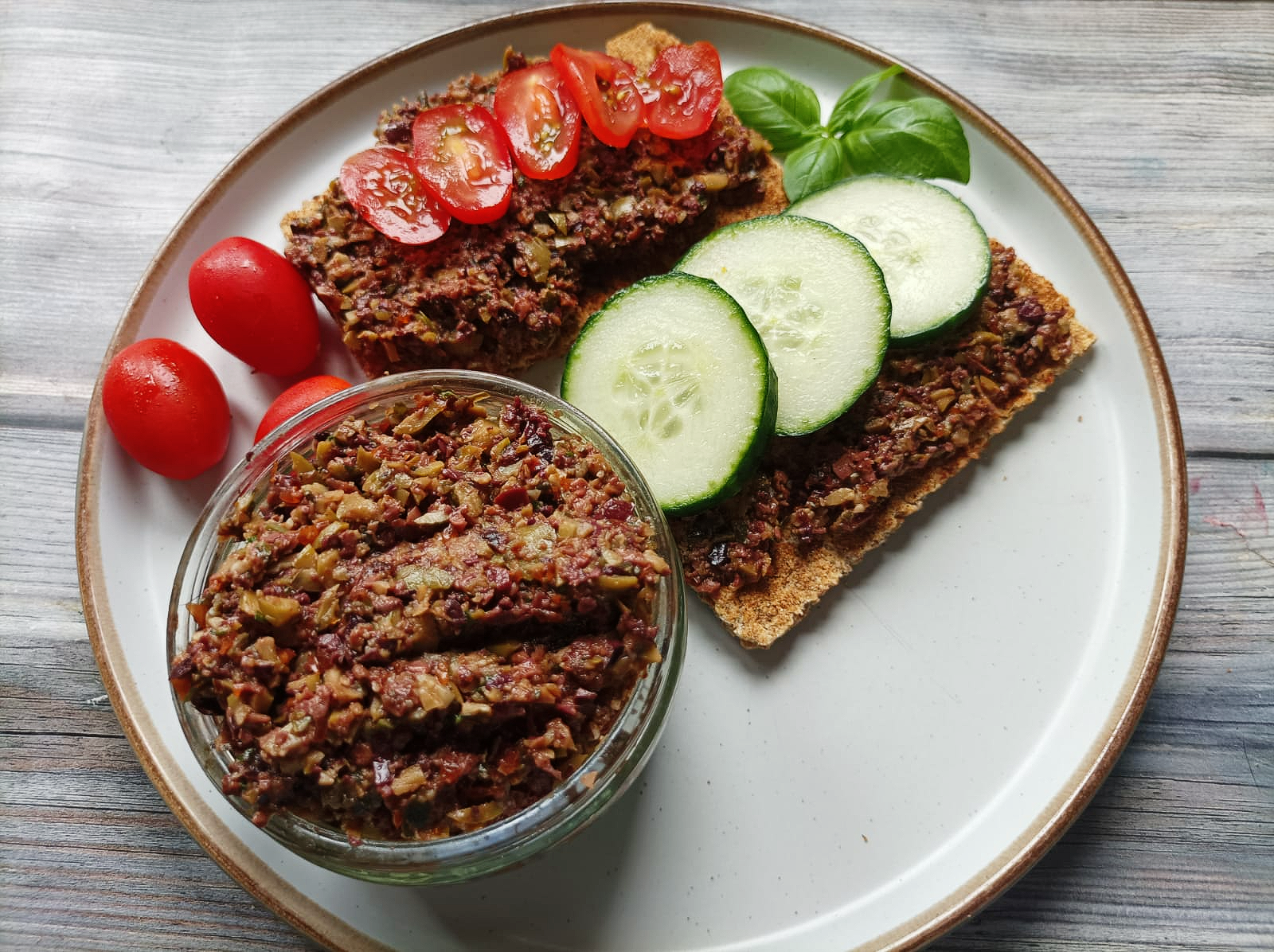 tapenade on a plate with rye crackers with cucumber and tomatoes