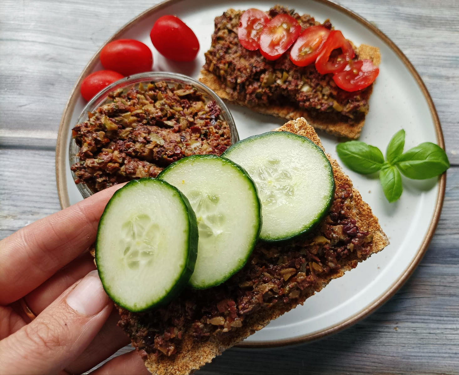 tapenade on a plate with rye crackers with cucumber and tomatoes
