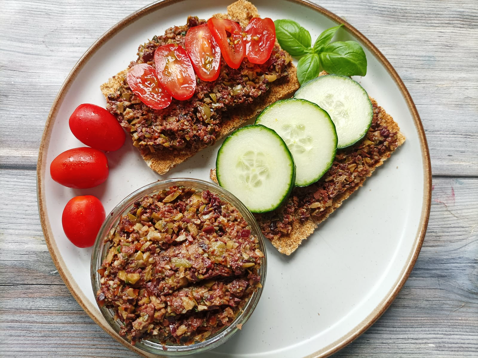 tapenade on a plate with rye crackers with cucumber and tomatoes