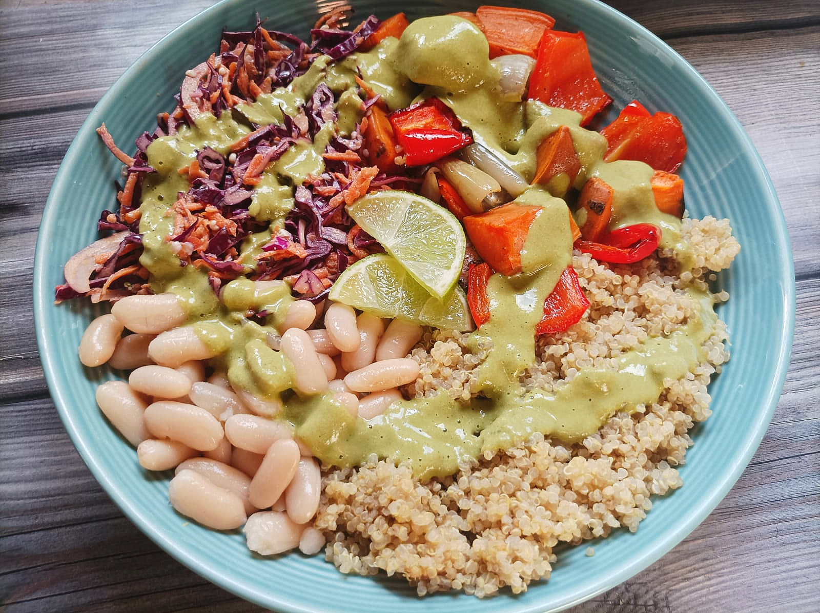 buddha bowl with slaw, beans, quinoa, roasted veggies, and green sauce. Topped with lime slices