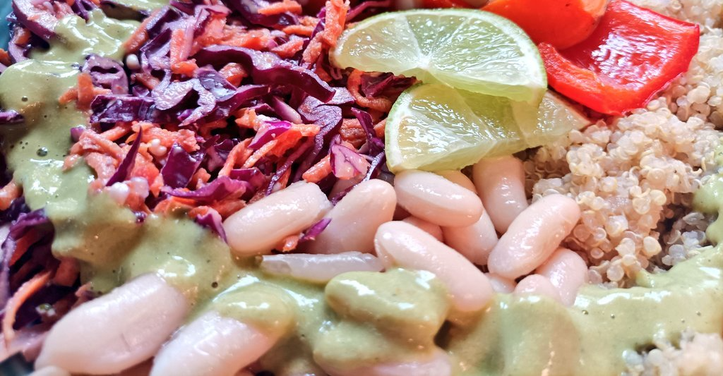 buddha bowl with slaw, beans, quinoa, roasted veggies, and green sauce. Topped with lime slices