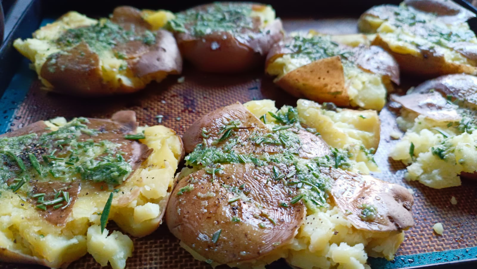 squashed potatoes on a baking tray with rosemary and garlic paste
