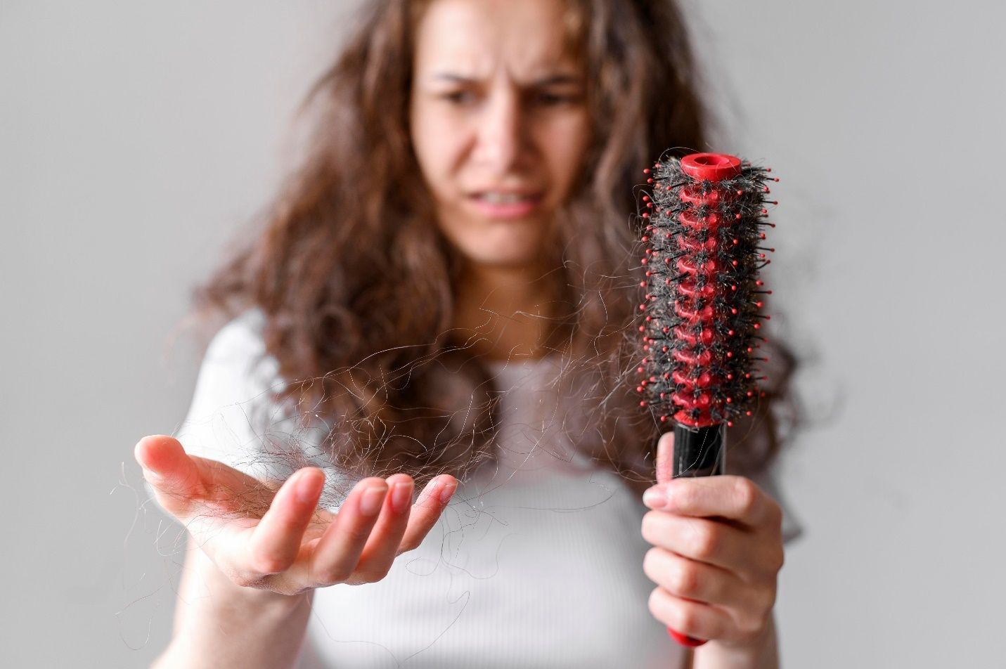a lady holding a brush in one hand and a clump of hair in the other to suggest hair loss.