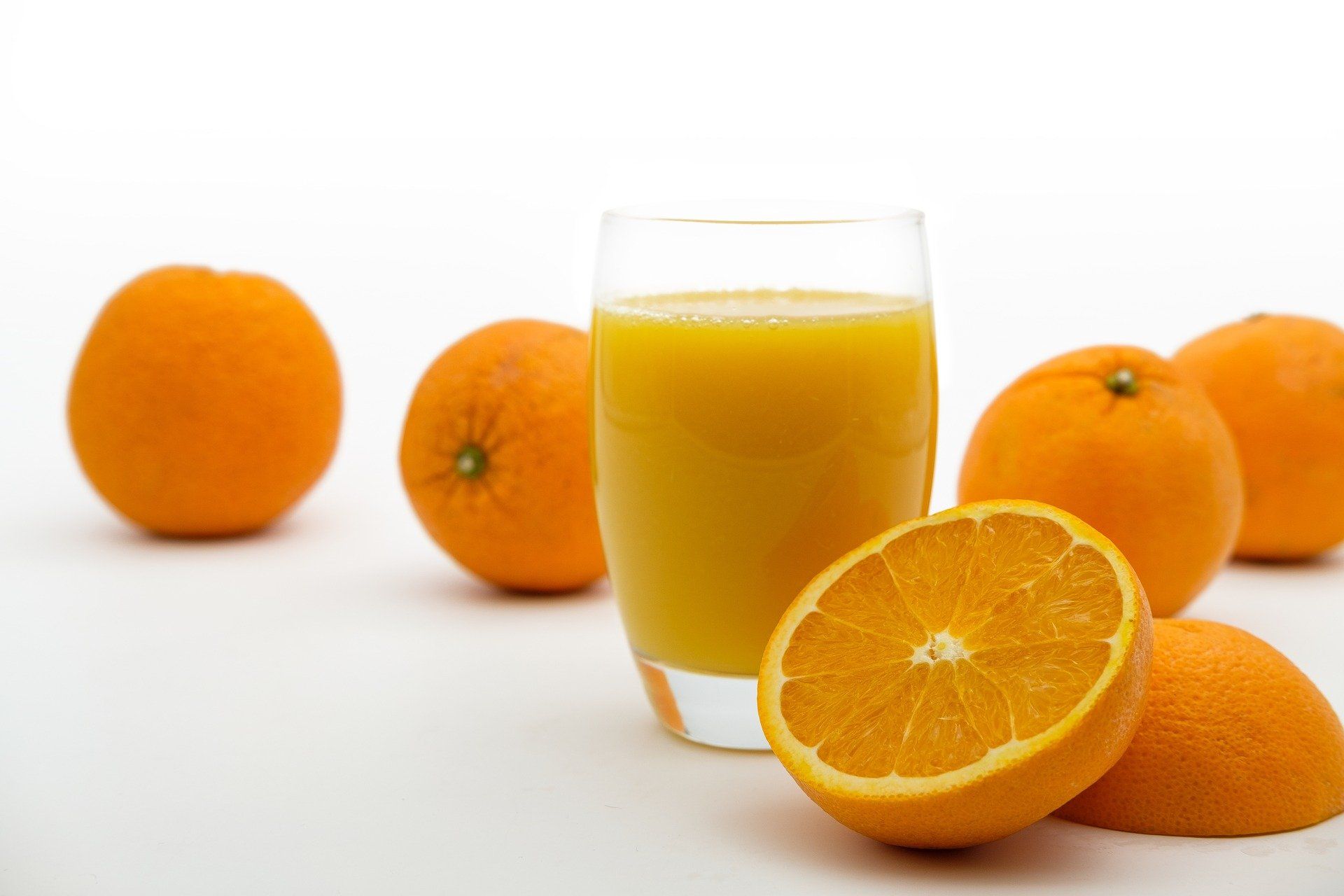 Fresh orange juice in a glass next to a cut orange and oranges in the background