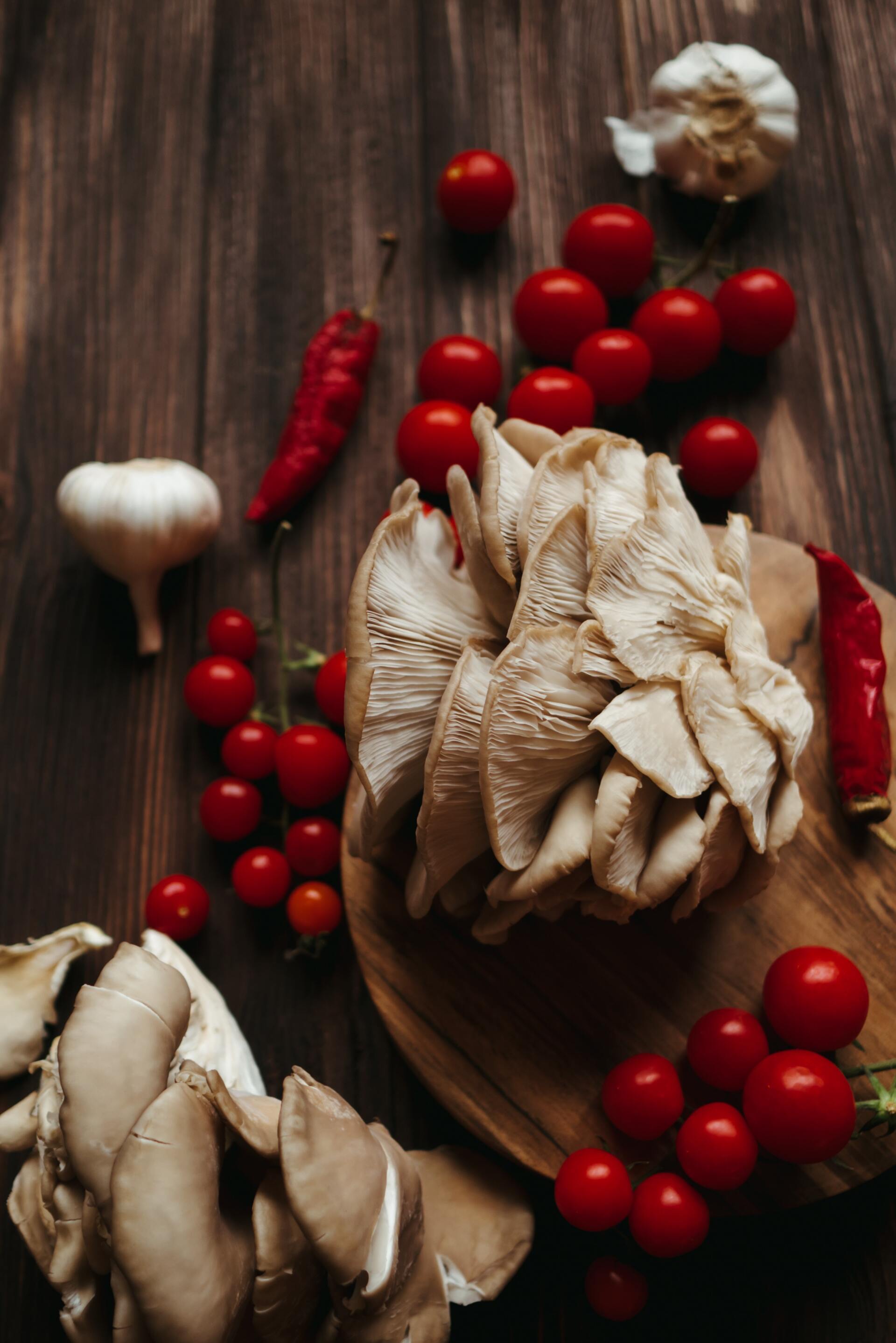 oyster mushrooms on a chopping board with bright red chili and tomatoes
