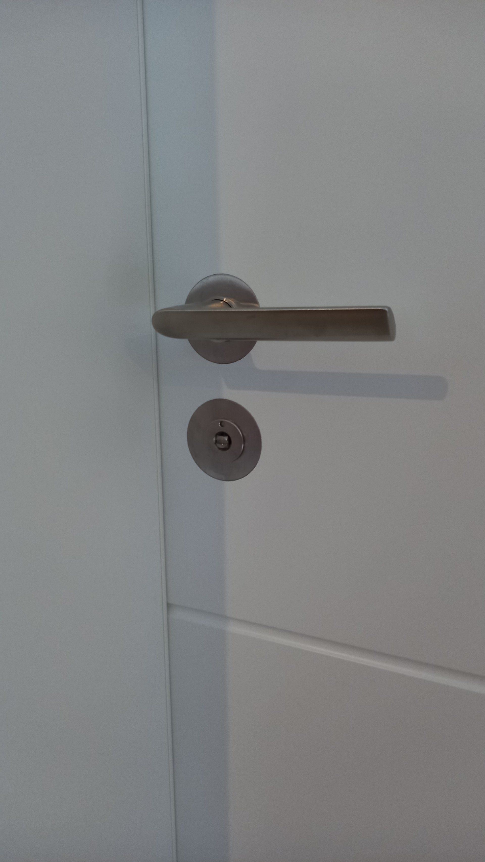 Detail Türklinke mit flächenbündigen Rosetten bündig eingelassen an weiß lackierter Zimmertüre mit Fräsrille