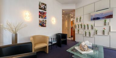 Moderner Empfangsbereich mit TV, Pflanzen und Informationsmaterialien an der Wand. MedicaDenta Wartezimmer