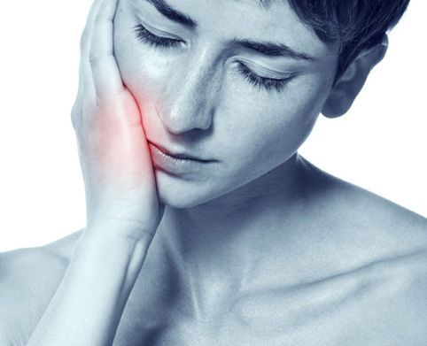 Patientin hält die Hand an die schmerzende Wange vor einer Behandlung