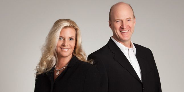 Ein Zahnarzt und eine Zahnärztin in eleganter, schwarzer Kleidung, stehen freundlich nebeneinander