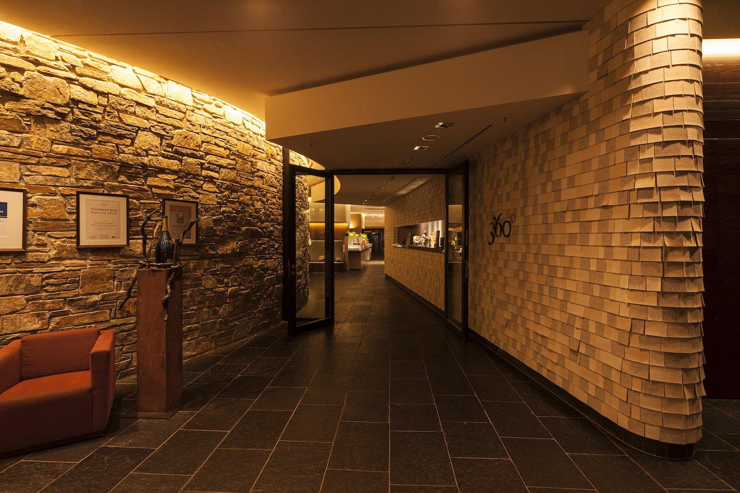 Im Eingangsbereich zum Restaurant werden Wandflächen repräsentativ inszeniert – Am Morgen empfängt die mit Filzschindeln verkleidete, hell und freundlich beleuchtete Wand den Frühstücksgast, am Abend die mit Streiflicht in ihrer Dreidimensionalität betonte Natursteinwand zum Dinner. / Foto alexandralechner.de