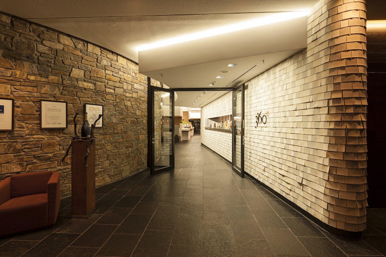 Im Eingangsbereich zum Restaurant werden Wandflächen repräsentativ inszeniert – Am Morgen empfängt die mit Filzschindeln verkleidete, hell und freundlich beleuchtete Wand den Frühstücksgast, am Abend die mit Streiflicht in ihrer Dreidimensionalität betonte Natursteinwand zum Dinner / Foto alexandralechner.de