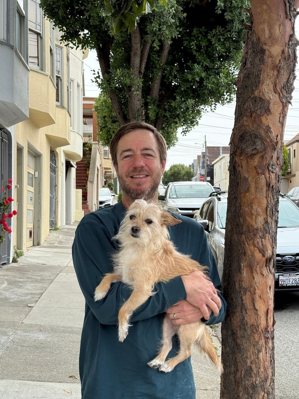 Arlo and his dog Rex are standing under a tree next to a street in San Francisco.