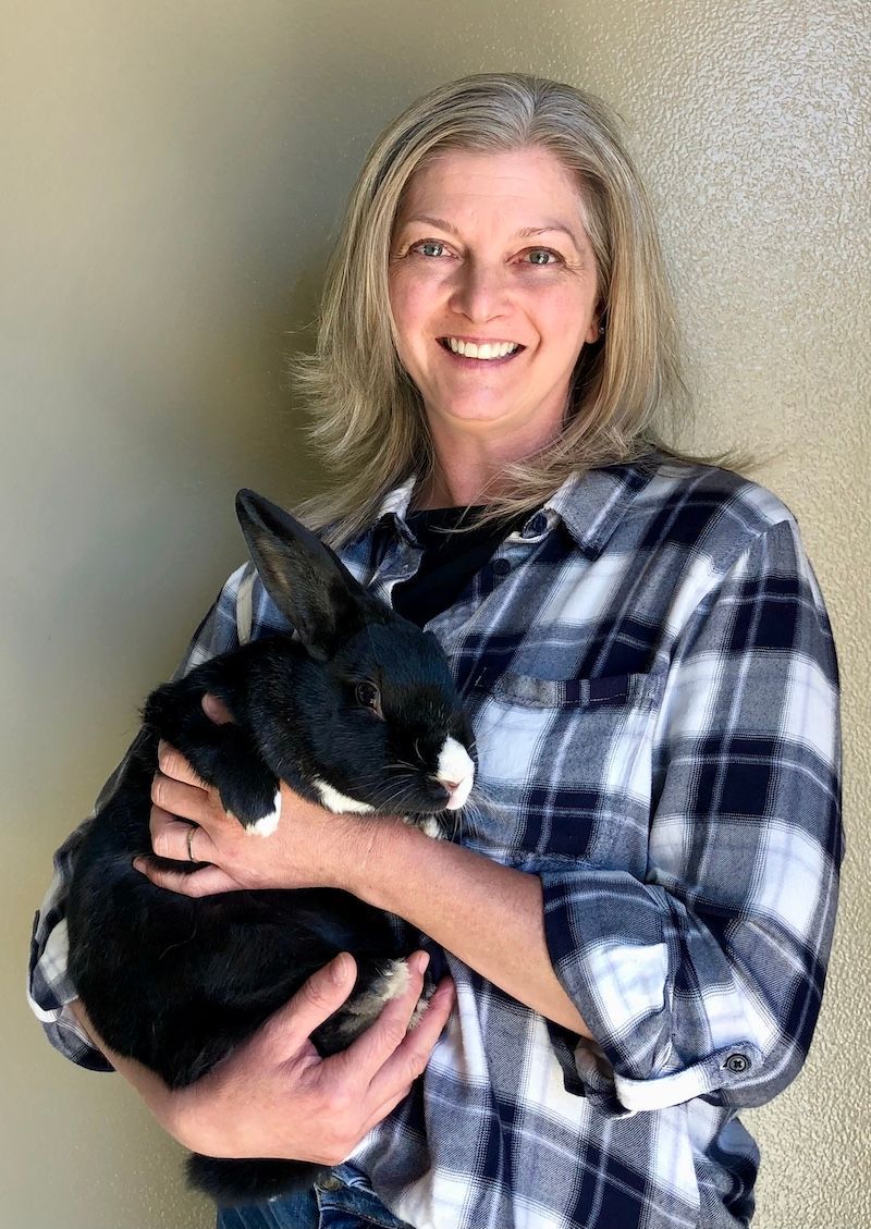 Brenda Melton smiles warmly as she cradles a black bunny in her arms, wearing a blue plaid shirt.