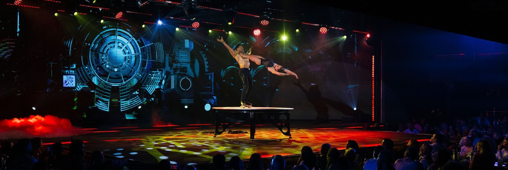 Aerial artist performing above the stage with colorful lighting, scene from the Origen show by Are You Ready