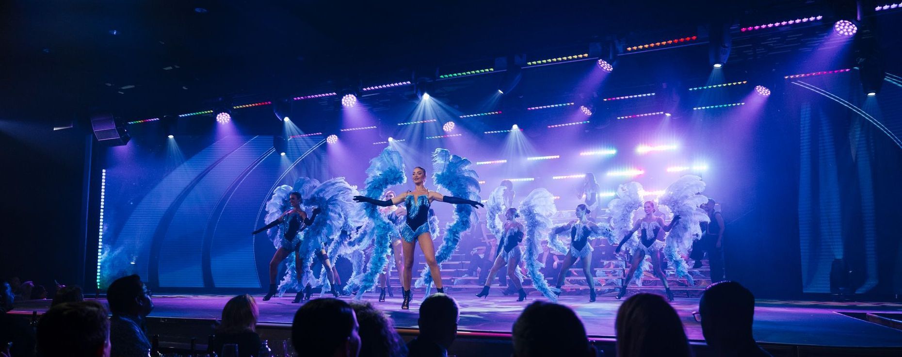 Cast performing a group dance in feathered costumes, scene from the Origen show by Are You Ready