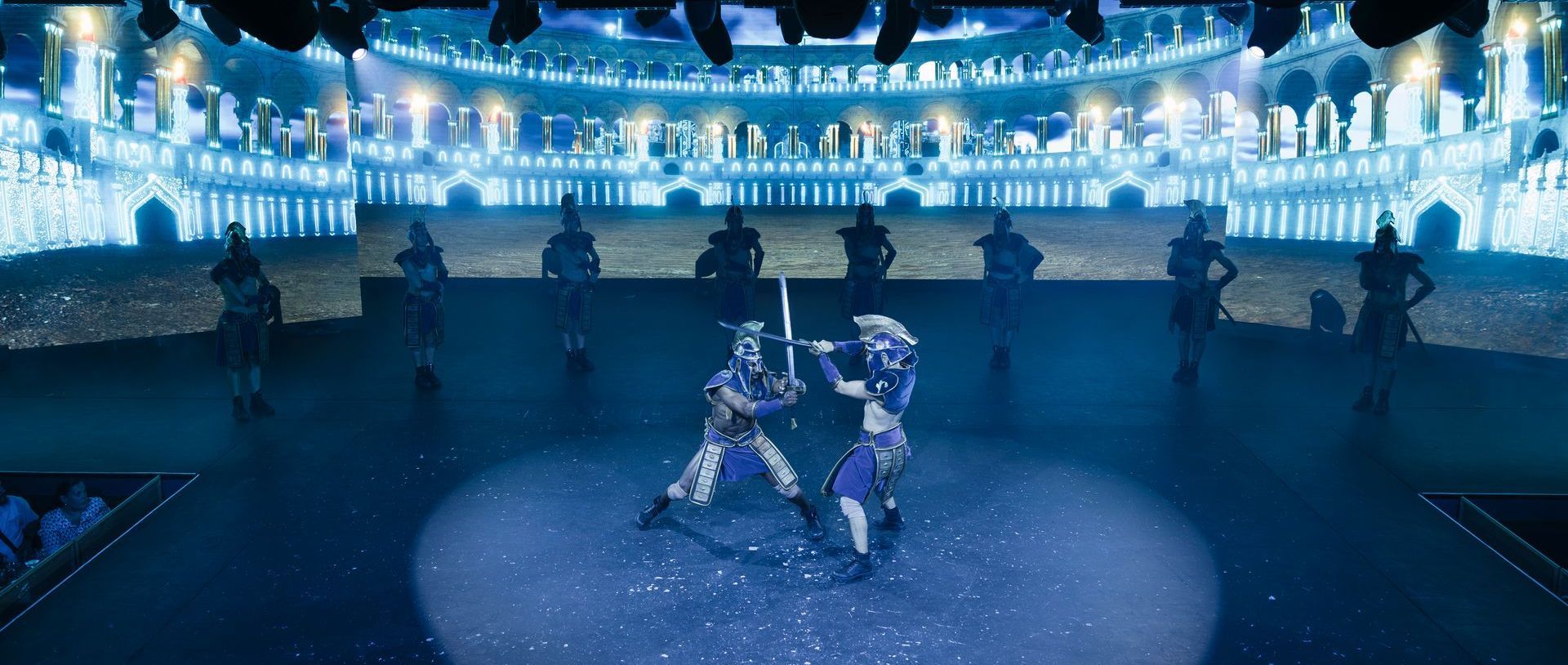 Escena de combate con espadas bajo luces azules durante el espectáculo Origen de Are You Ready