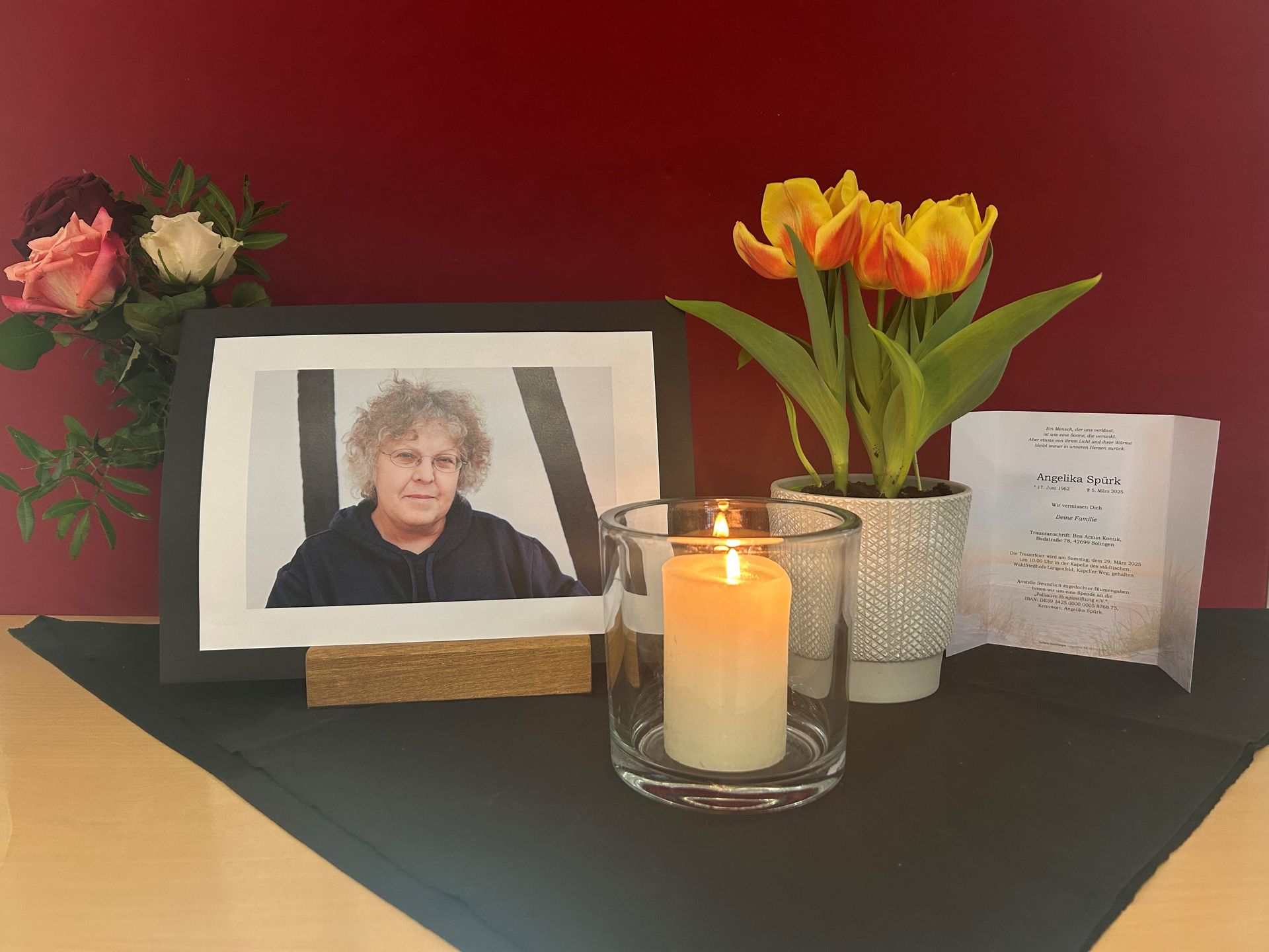 schwarz umrahmtes Foto von verstorbener Kollegin neben Blumen und brennender Kerze