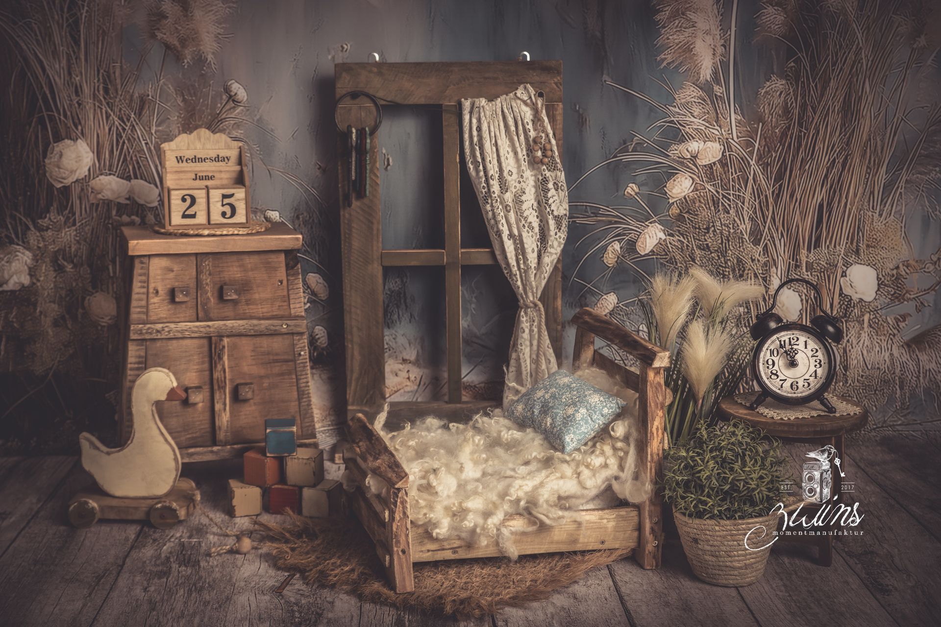 Fotoset für Neugeborene mit Holzbett und Kommode auf einem blauen Hintergrund mit Dünenpflanzen und einem Holzfenster