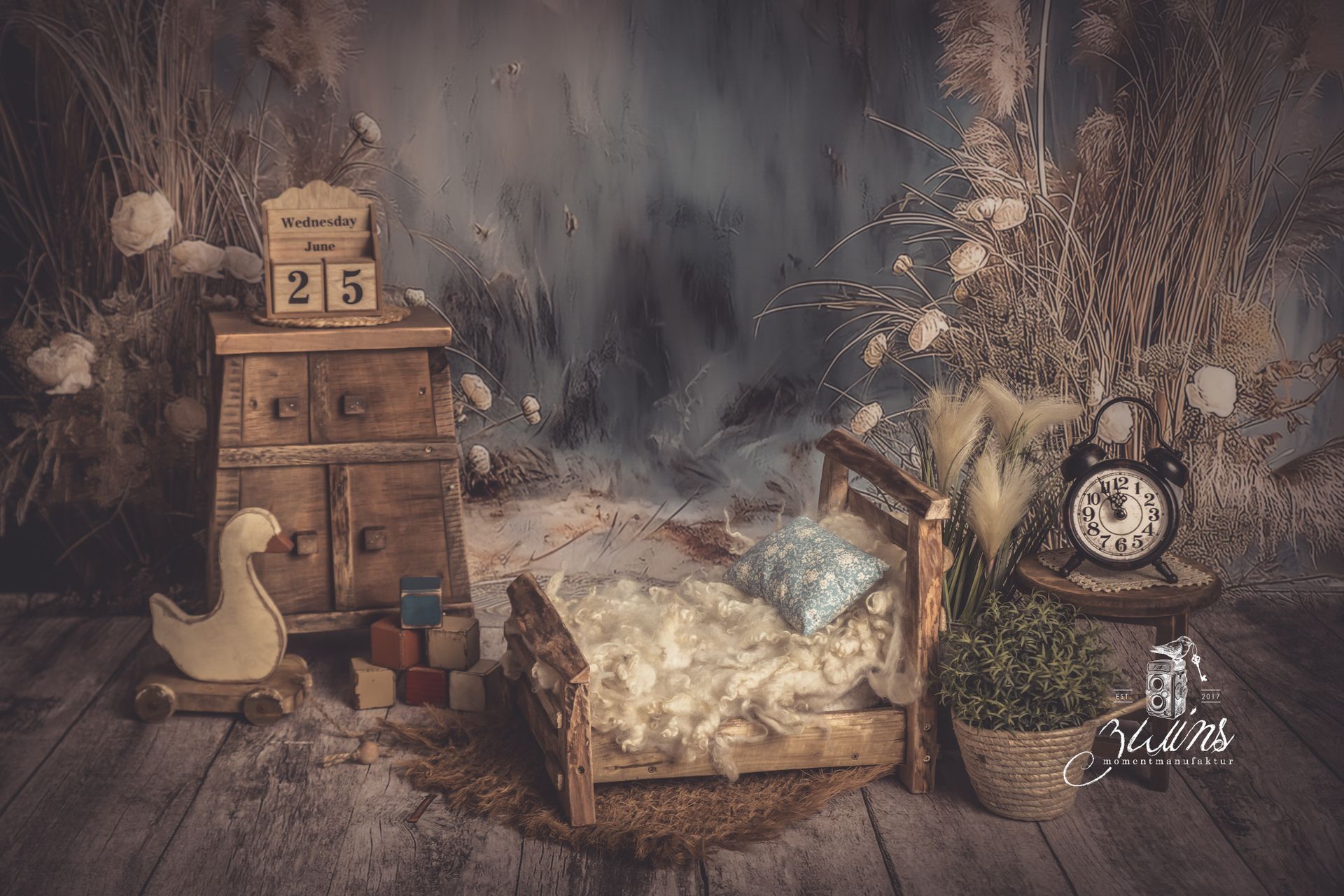 Fotoset für Neugeborene mit Holzbett und Kommode auf einem blauen Hintergrund mit Dünenpflanzen
