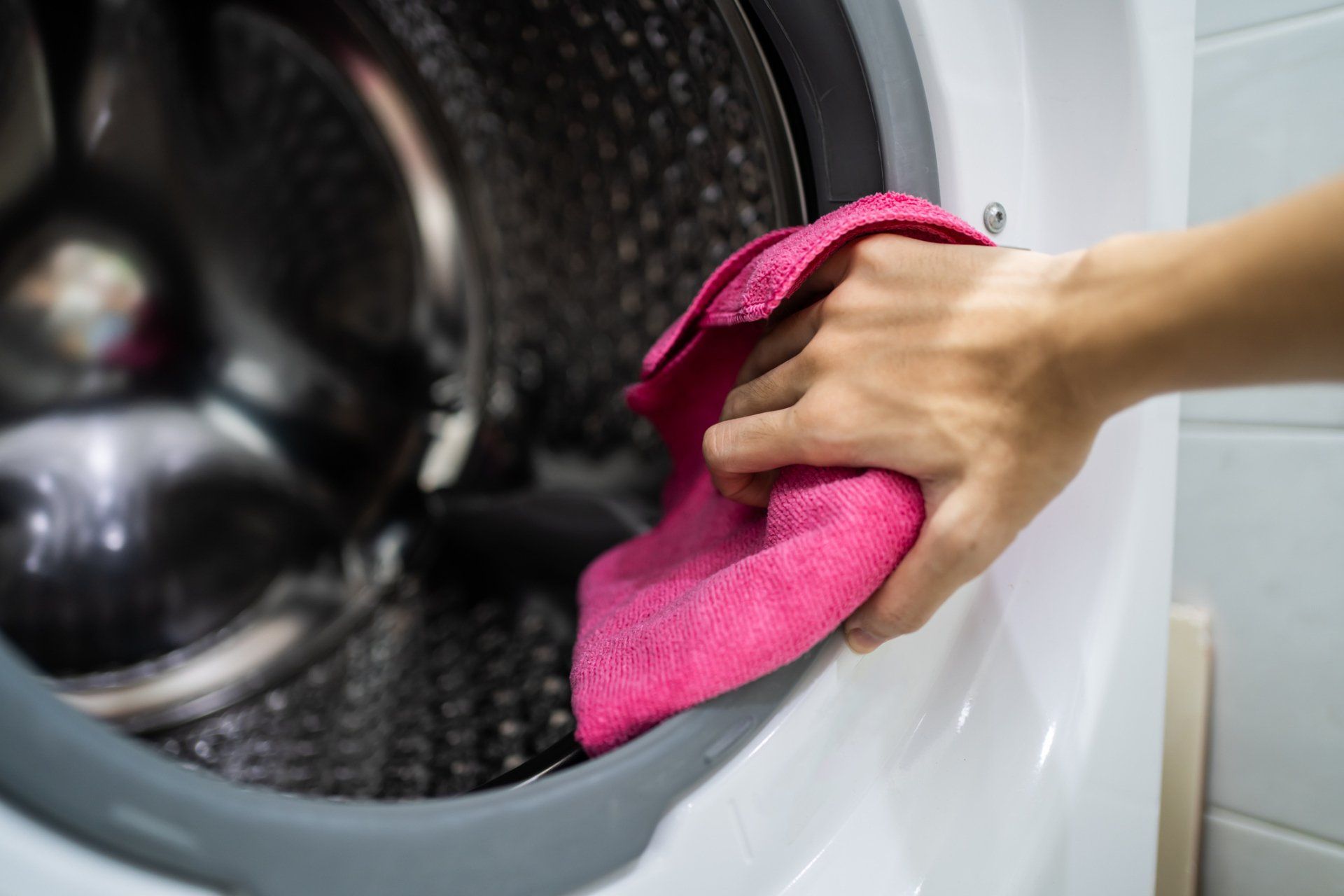 Frau reinigt die offene Waschmaschinentür mit einem Lappen – Tipps für die Pflege und Hygiene von Haushaltsgeräten.
