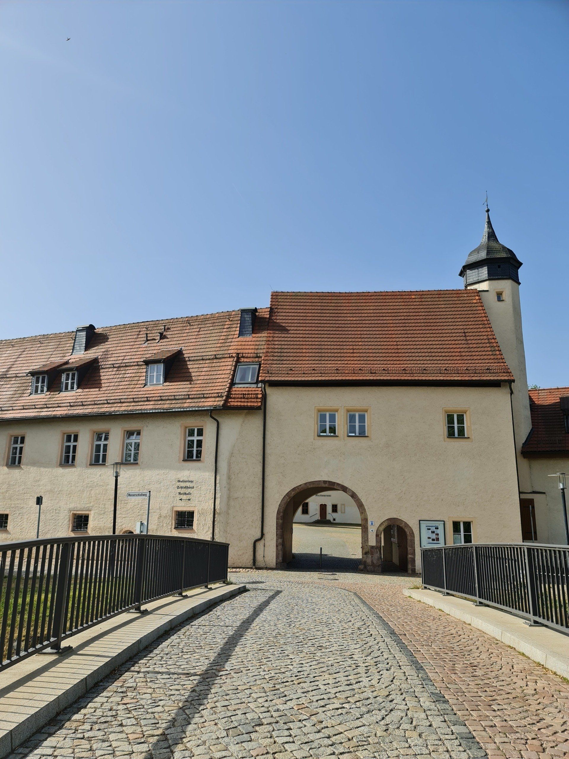 hinter der Brücke sehen wir die Wirtschaftsgebäude und die Toreinfahrt und einen Turm vom Wasserschloss Klaffenbach