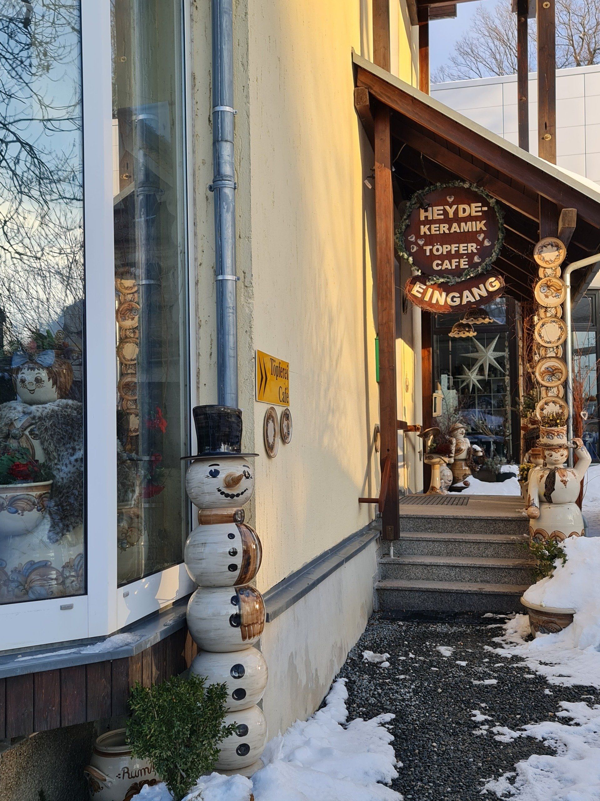 Eingang zur Töpferei mit großem Schneemann aus Keramik und anderen Figuren davor Schild über dem Eingang