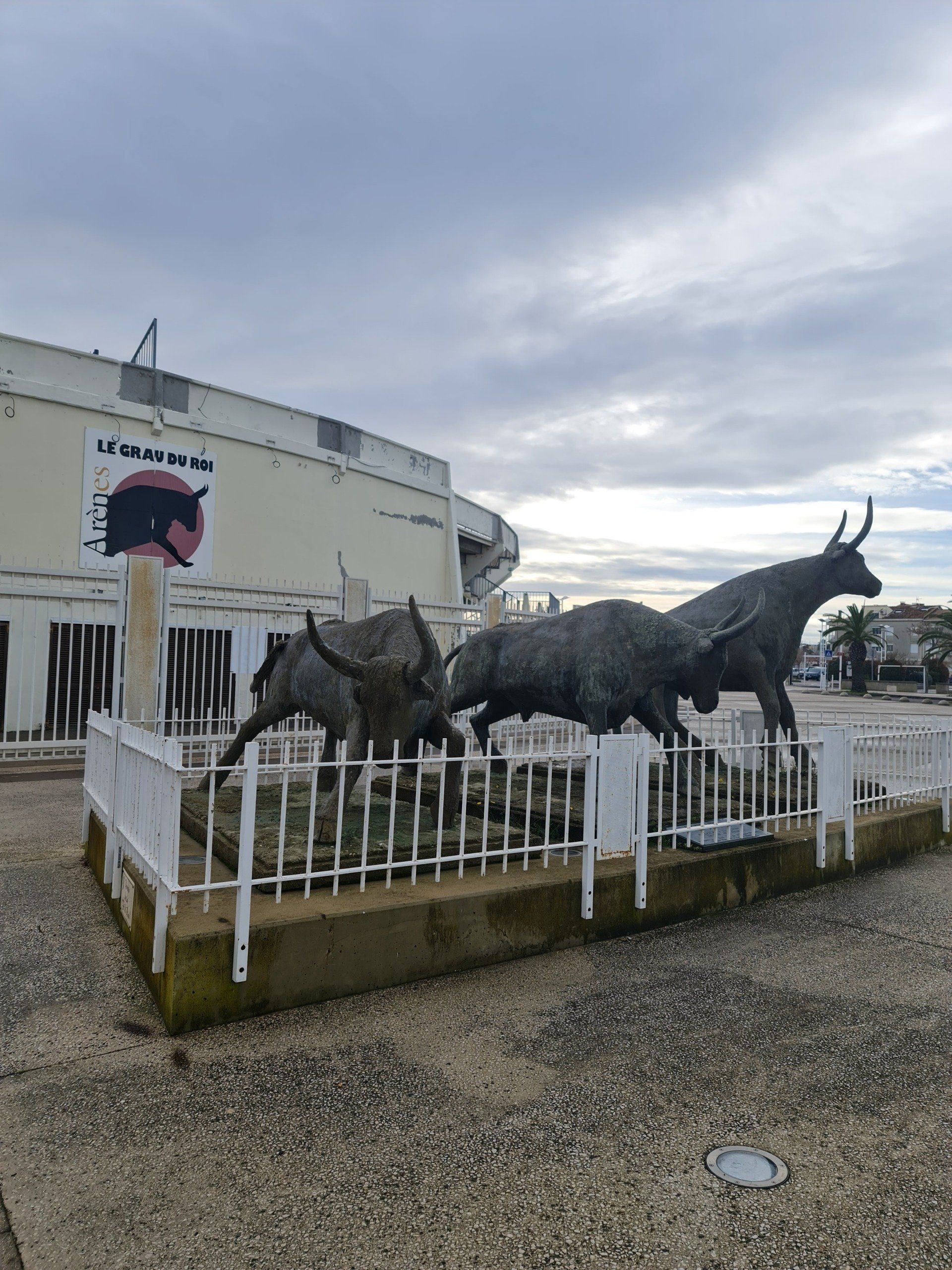 schwarze Stiere aus Metall vor einer runden, weißen  Arena