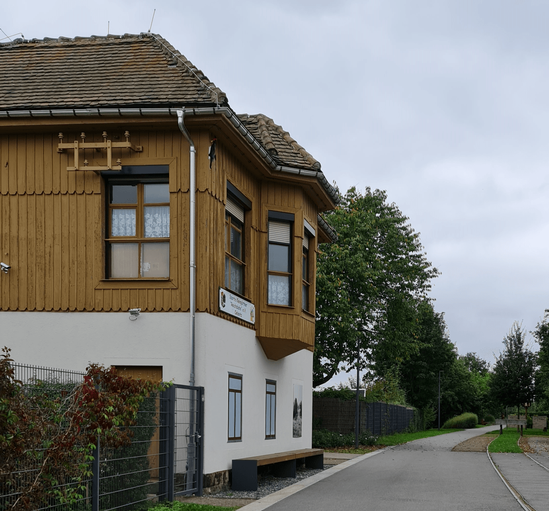 Die Zugstrecke endet hier - der Park geht noch weiter - auf Erkundungstour durch den Bürgerpark in Oelsnitz im Erzgebirge Photo by: Viola Einert-Krug Bahnwärterhäuschen weiß, mit Bankk davor, Metallzaun und Grüne Bäume im Hintergrund, Weg, die Gleise enden - Barke rechts