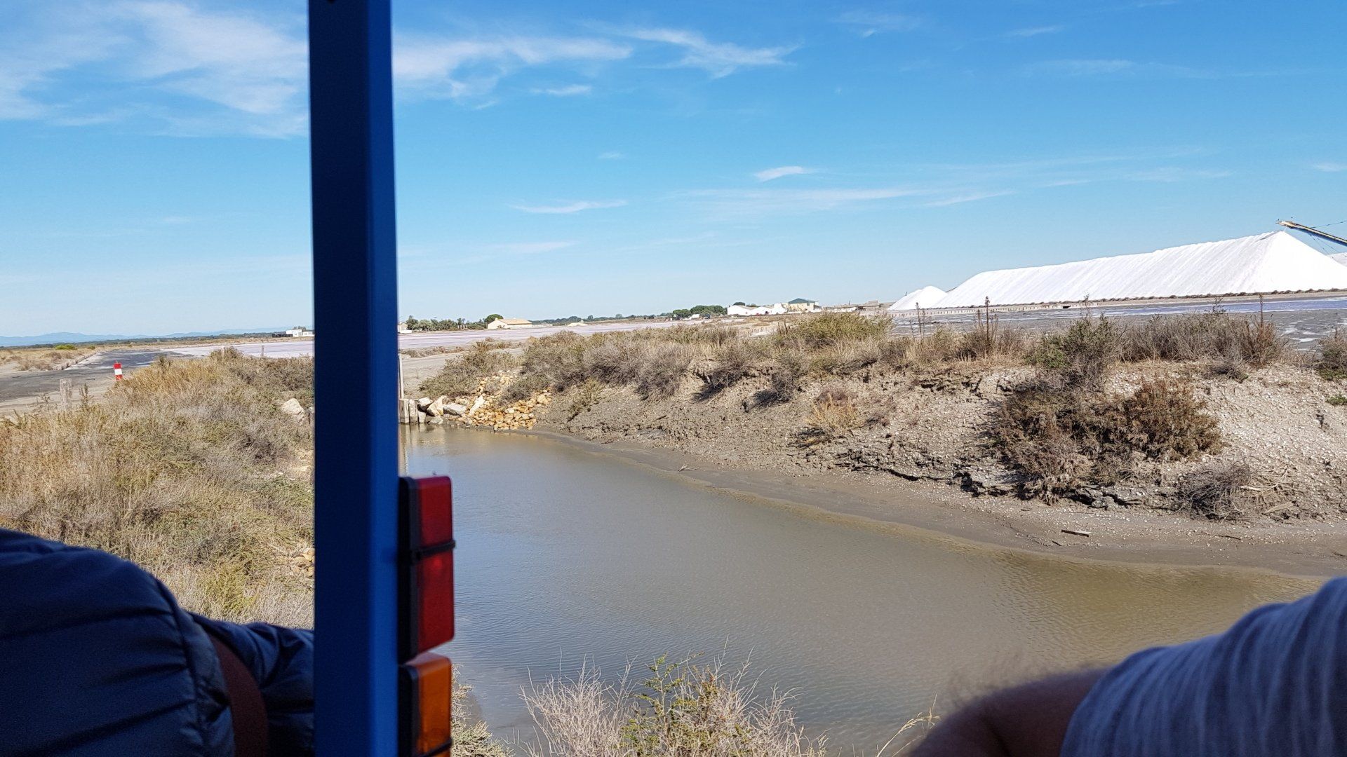 Bach und dahinter weite Landschaft der Salzsaline du Midi kleinen Gläschen darauf, in denen das Salz drin ist Auf der Tonne sind das Kreuz der Camargue und das weiße Camargue Pferd und die Burg von Auiges Mortes abgebildet