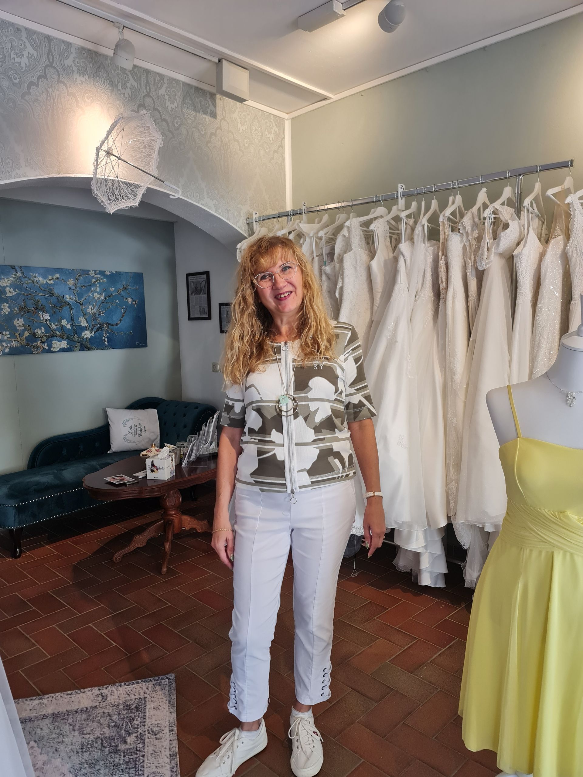 Inhaberin steht in ihrem Brautmodengeschäft vor schönen Kleidern.