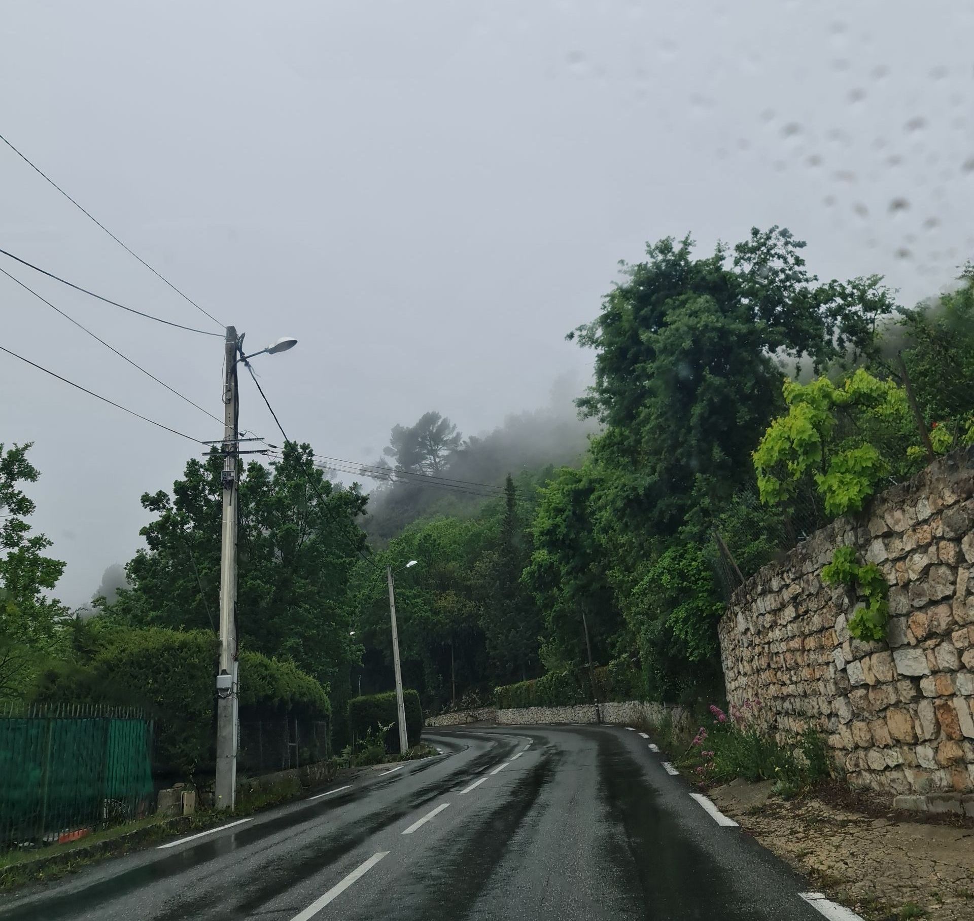 Eine Bergstraße im Regen gesäumt von Mauern und Bäumen